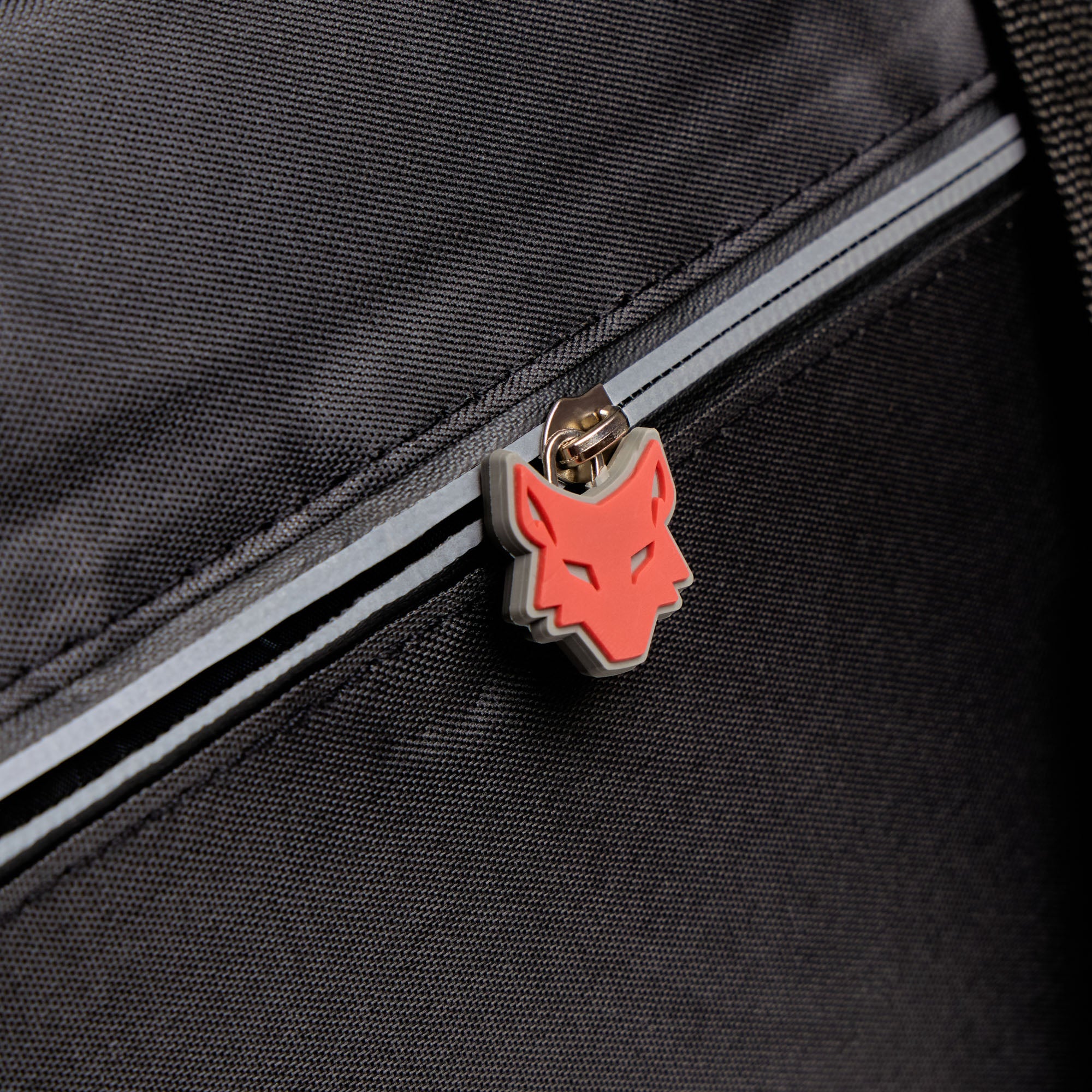 Close-up of a black bag with a red wolf emblem on a zipper