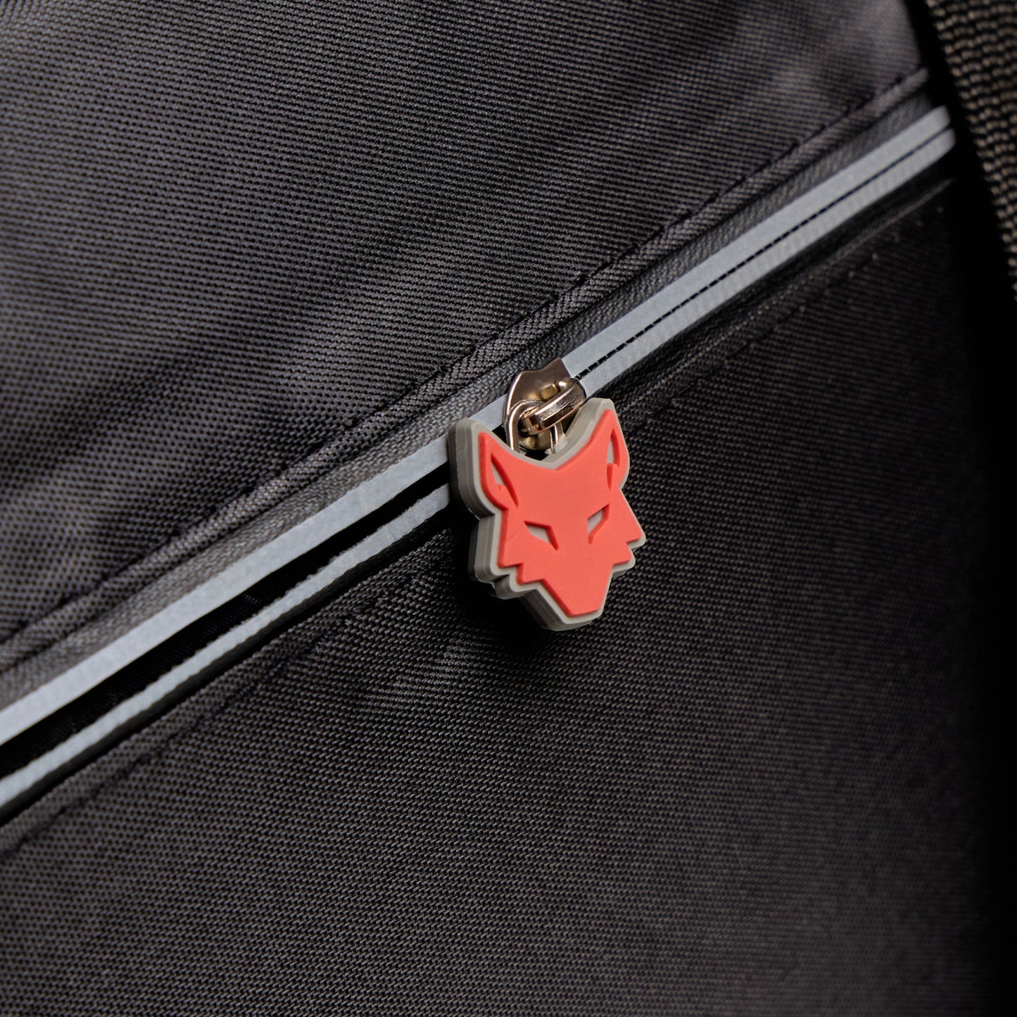 Close-up of a black bag with a red wolf emblem on a zipper