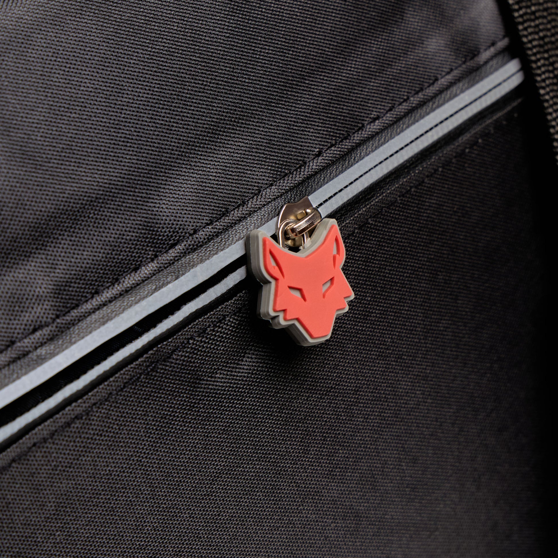 Close-up of a black bag with a red wolf emblem on a zipper